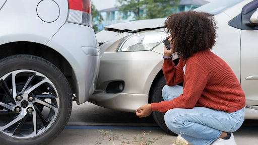 What to do after a minor car accident – Woman crouched down inspecting her car after an accident